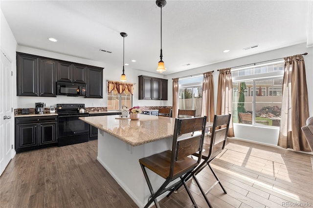 kitchen featuring light stone counters, wood finished floors, visible vents, black appliances, and a kitchen bar