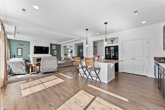 kitchen with visible vents, a breakfast bar, a stone fireplace, wood finished floors, and hanging light fixtures