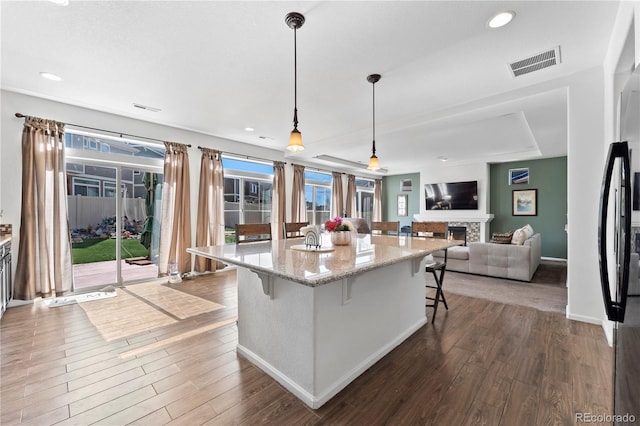 kitchen featuring dark wood finished floors, visible vents, a breakfast bar, and a lit fireplace