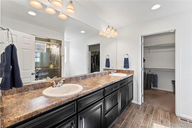 full bath with a sink, a walk in closet, double vanity, and a shower stall