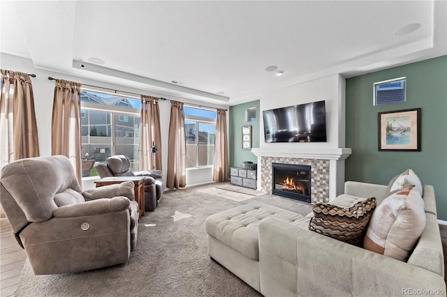 living room with a raised ceiling, carpet flooring, and a glass covered fireplace