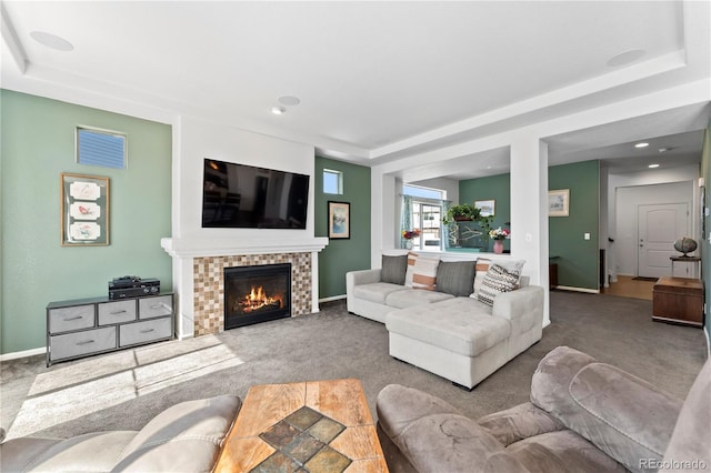 carpeted living area featuring a tiled fireplace, baseboards, and a raised ceiling