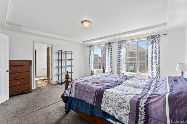 carpeted bedroom with ensuite bathroom, visible vents, and a raised ceiling