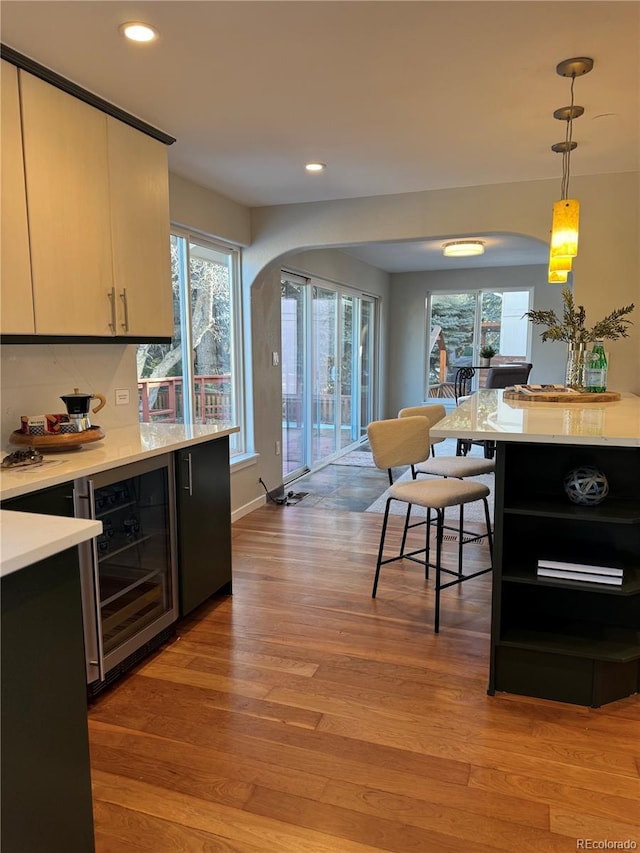 kitchen featuring a breakfast bar, pendant lighting, wine cooler, and light hardwood / wood-style flooring