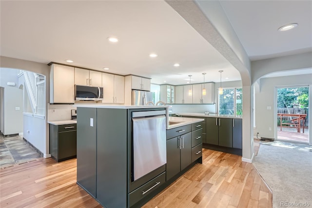 kitchen with pendant lighting, light hardwood / wood-style flooring, stainless steel appliances, and an island with sink