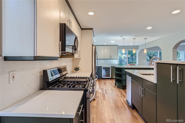 kitchen featuring decorative light fixtures, sink, wine cooler, stainless steel appliances, and a center island with sink