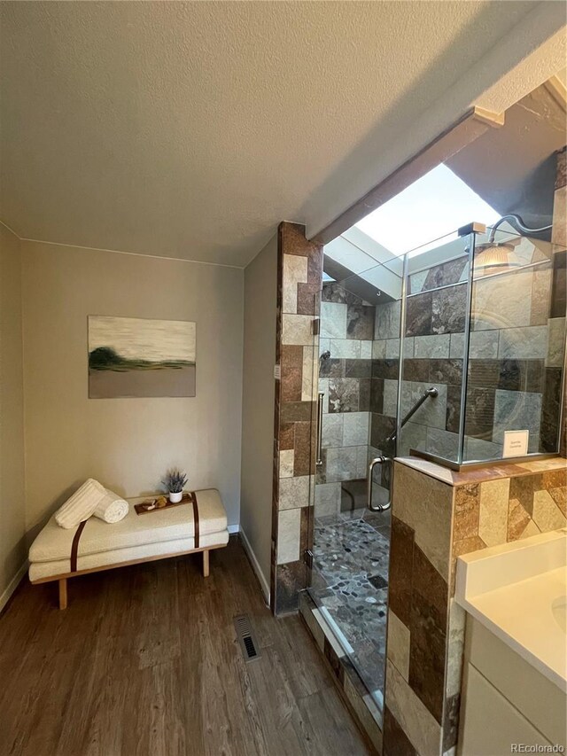 bathroom with hardwood / wood-style flooring, vaulted ceiling, vanity, a textured ceiling, and a shower with shower door