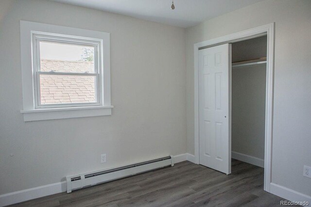 unfurnished bedroom with baseboards, dark wood-type flooring, baseboard heating, and a closet