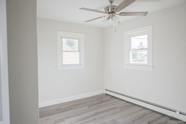 spare room featuring a healthy amount of sunlight, a baseboard heating unit, baseboards, and wood finished floors