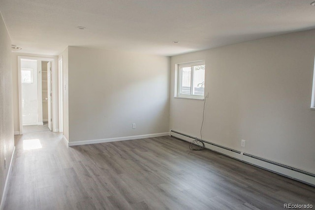 empty room featuring a baseboard heating unit, baseboards, and wood finished floors