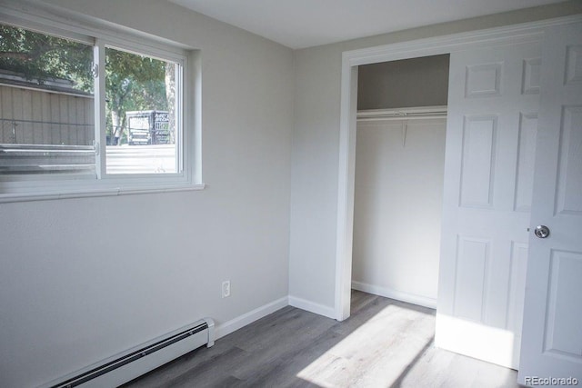 unfurnished bedroom with baseboards, wood finished floors, a closet, and a baseboard radiator