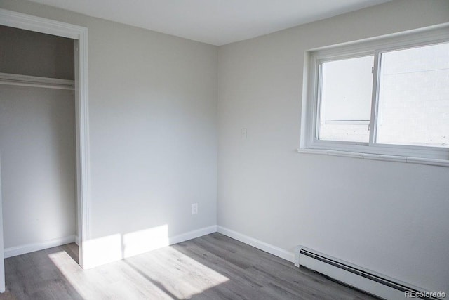 unfurnished bedroom with a baseboard heating unit, baseboards, a closet, and wood finished floors