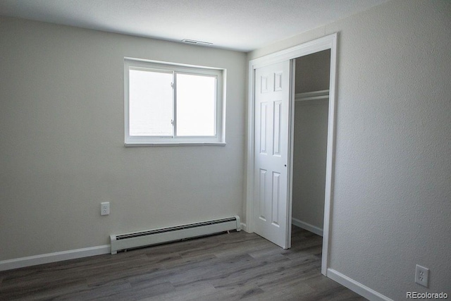 unfurnished bedroom featuring visible vents, baseboards, baseboard heating, wood finished floors, and a closet