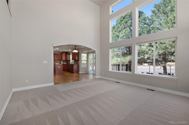 7436 Centennial Glen Dr, Colorado Springs, CO 80919 - unfurnished living room featuring light carpet, a towering ceiling, arched walkways, and baseboards