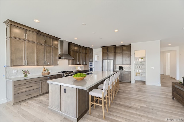 kitchen featuring an island with sink, wall chimney range hood, decorative backsplash, and appliances with stainless steel finishes