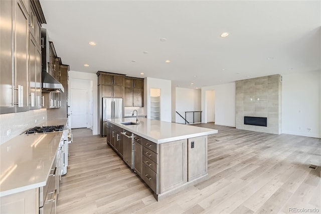 kitchen featuring stainless steel appliances, light hardwood / wood-style flooring, sink, a fireplace, and a large island with sink