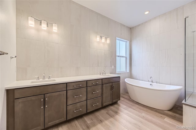 bathroom with hardwood / wood-style floors, independent shower and bath, vanity, and tile walls