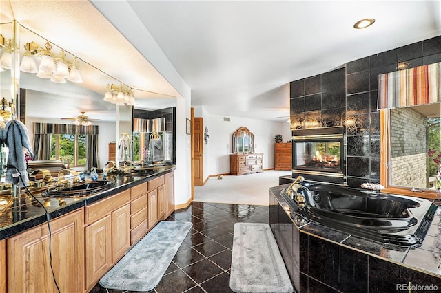 bathroom with a tile fireplace, ceiling fan, tile patterned flooring, tiled bath, and vanity