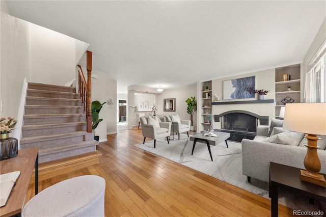 living area with a fireplace, built in features, baseboards, light wood-style floors, and stairs