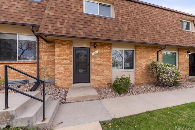 doorway to property with roof with shingles, brick siding, and mansard roof