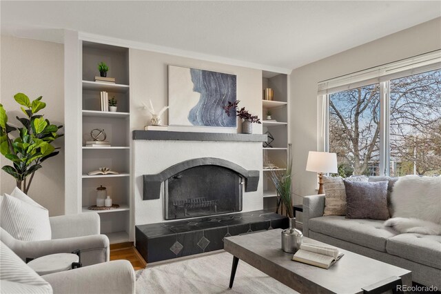 living area featuring a tile fireplace, wood finished floors, and built in shelves