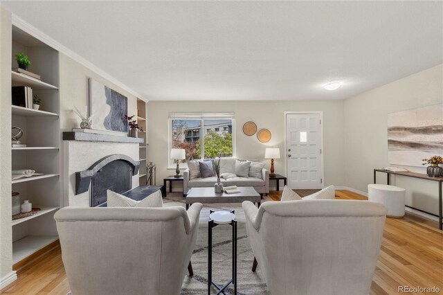 living area featuring a fireplace, light wood-style flooring, and built in features