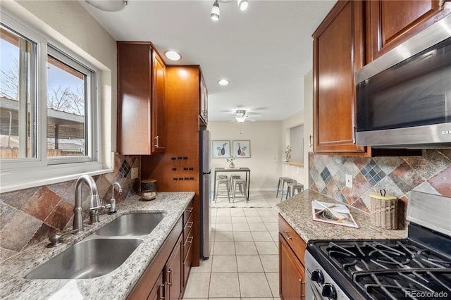 kitchen featuring a sink, brown cabinets, decorative backsplash, light tile patterned floors, and appliances with stainless steel finishes