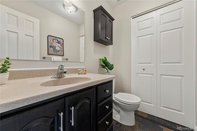 bathroom with vanity, toilet, a closet, and stone finish flooring