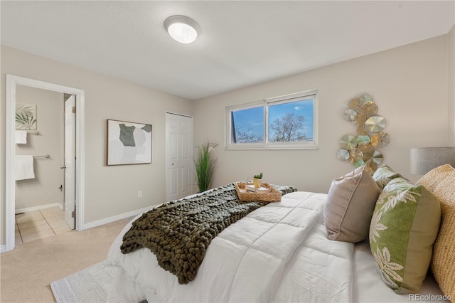 bedroom with baseboards, a closet, ensuite bath, and light colored carpet