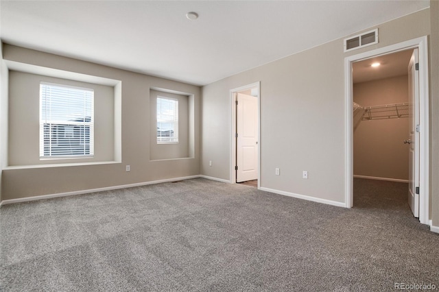 unfurnished bedroom with multiple windows, a spacious closet, dark carpet, and a closet