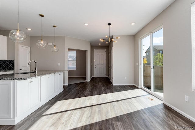 kitchen with white cabinets, light stone countertops, pendant lighting, dark hardwood / wood-style floors, and sink