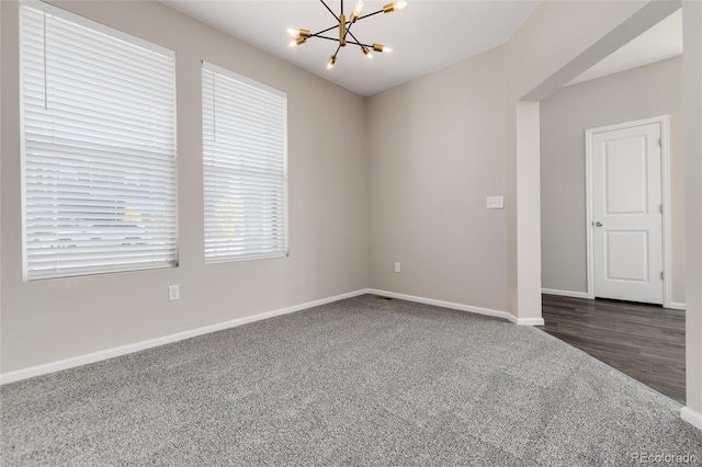 empty room featuring dark carpet and a notable chandelier