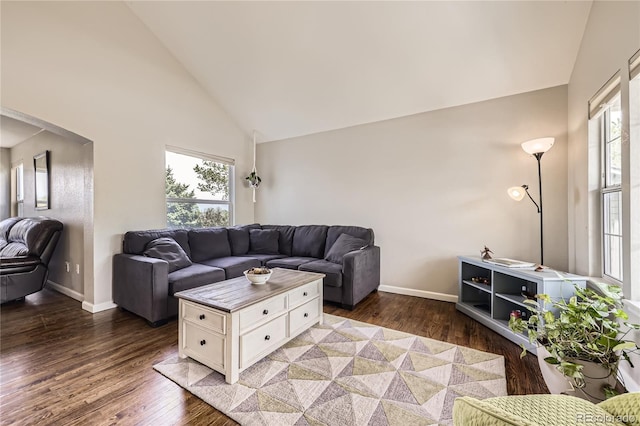 living area with high vaulted ceiling, arched walkways, wood finished floors, and baseboards
