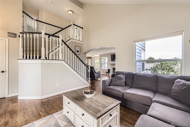 living room with arched walkways, stairway, wood finished floors, a high ceiling, and baseboards