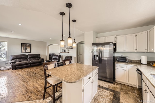 kitchen featuring stainless steel fridge, arched walkways, white cabinets, light stone counters, and a center island