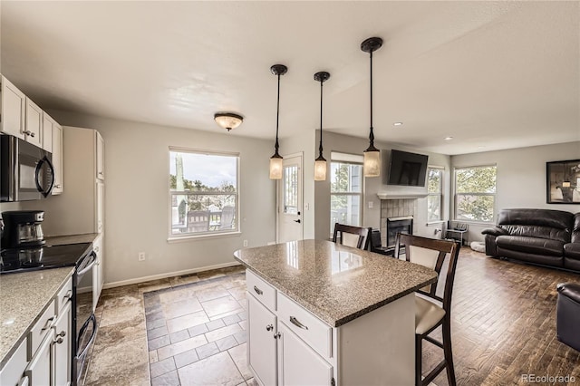 kitchen with black microwave, electric range oven, a tiled fireplace, a kitchen breakfast bar, and baseboards