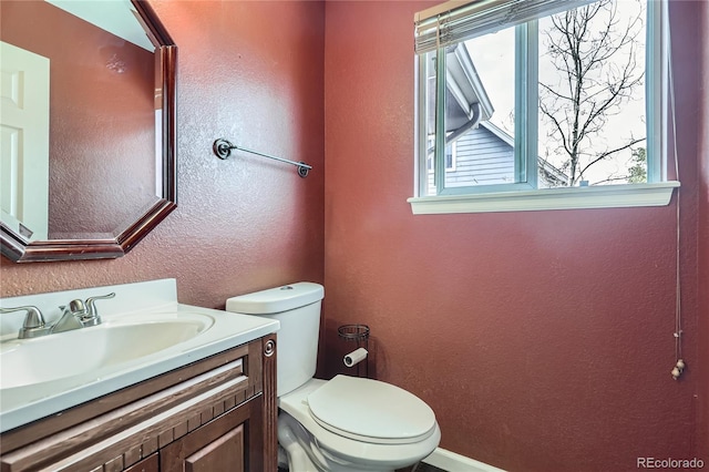 half bathroom featuring a textured wall, toilet, vanity, and baseboards
