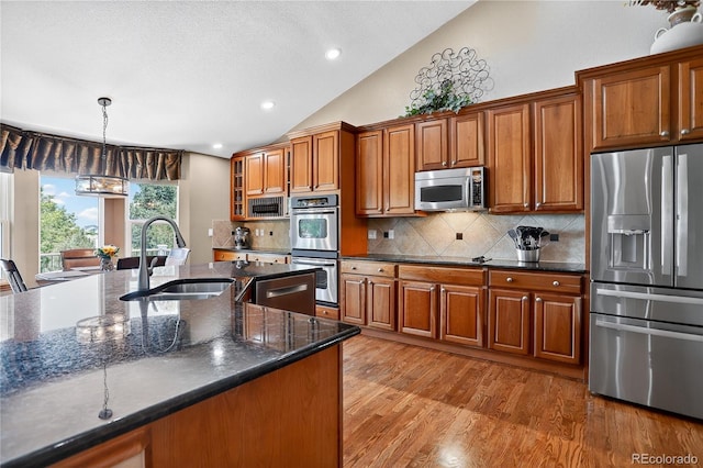 34827 E 7th Ave, Watkins, CO 80137 - kitchen with stainless steel appliances, brown cabinetry, lofted ceiling, light wood-style floors, and backsplash