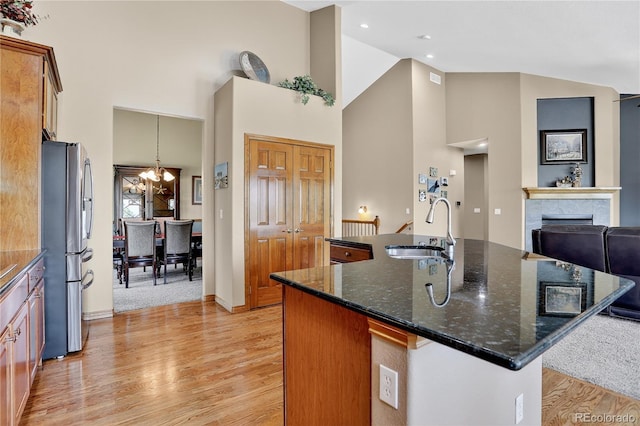 34827 E 7th Ave, Watkins, CO 80137 - kitchen featuring freestanding refrigerator, light wood-style flooring, high vaulted ceiling, dark stone counters, and a center island with sink