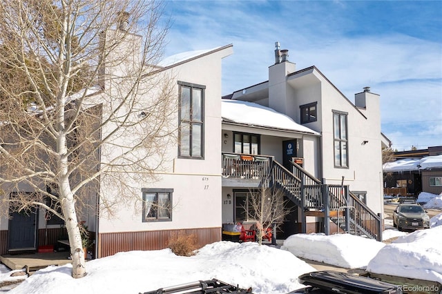 view of front of property featuring stairs, a chimney, and stucco siding