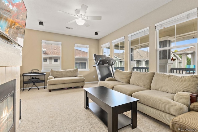 living room with baseboards, visible vents, a ceiling fan, a tile fireplace, and carpet flooring