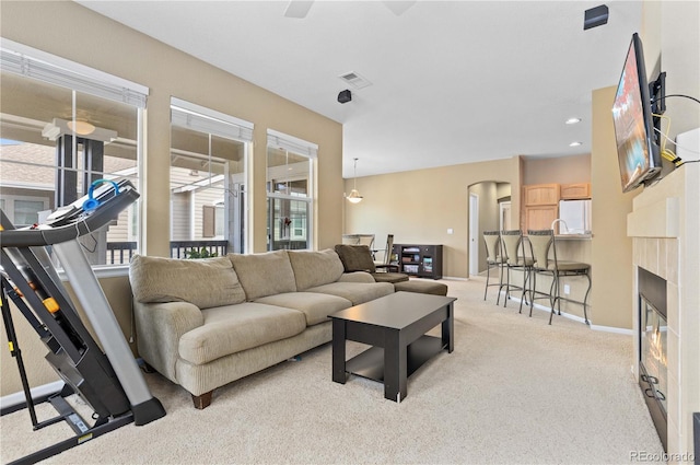 living area with visible vents, arched walkways, baseboards, light colored carpet, and a glass covered fireplace