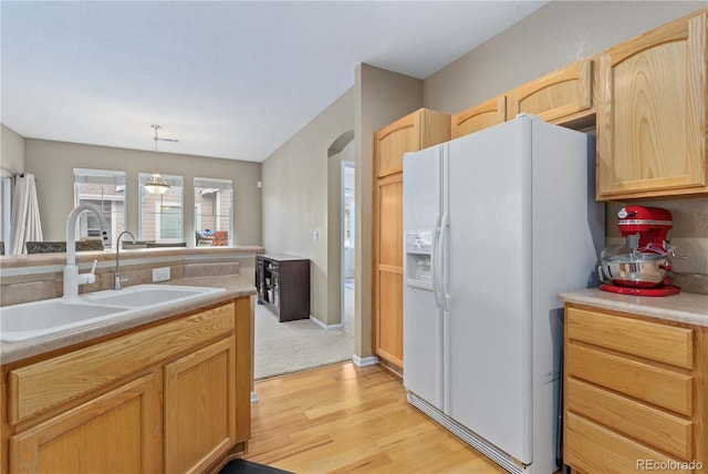 kitchen featuring arched walkways, white refrigerator with ice dispenser, light countertops, light brown cabinets, and a sink