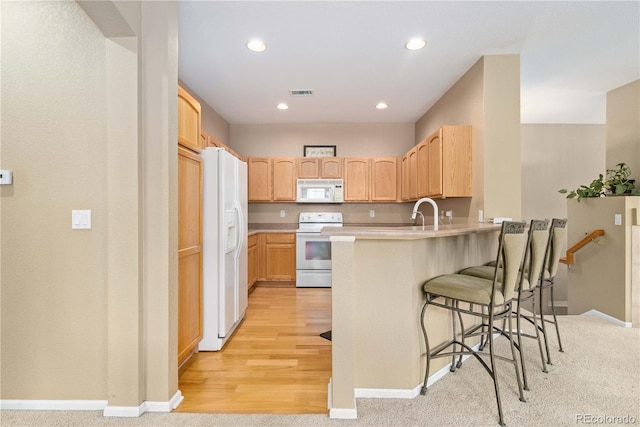 kitchen with white appliances, a breakfast bar area, a peninsula, light countertops, and light brown cabinets