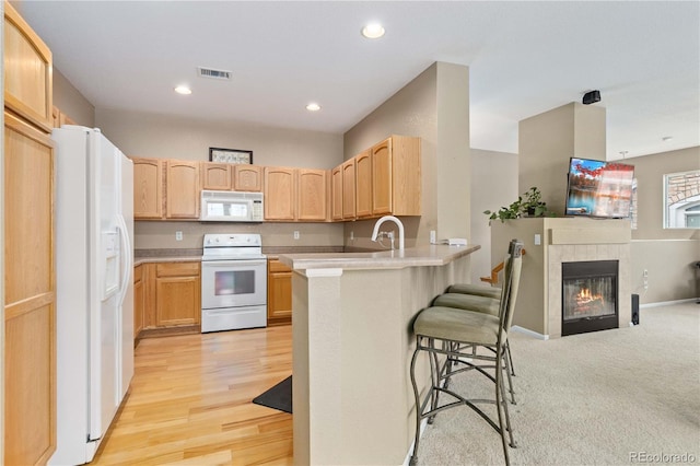 kitchen with a breakfast bar area, visible vents, light brown cabinets, white appliances, and a peninsula