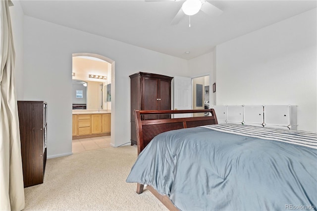 bedroom featuring arched walkways, connected bathroom, light carpet, a ceiling fan, and baseboards