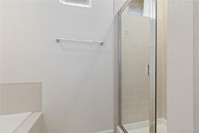 bathroom with a tub to relax in, a stall shower, and a textured wall