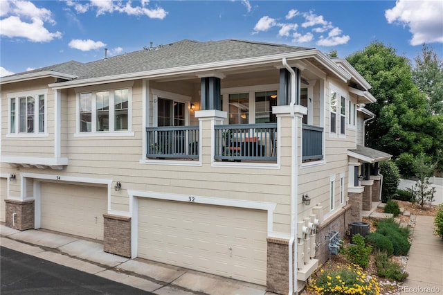 view of side of home with brick siding, a shingled roof, a balcony, a garage, and cooling unit