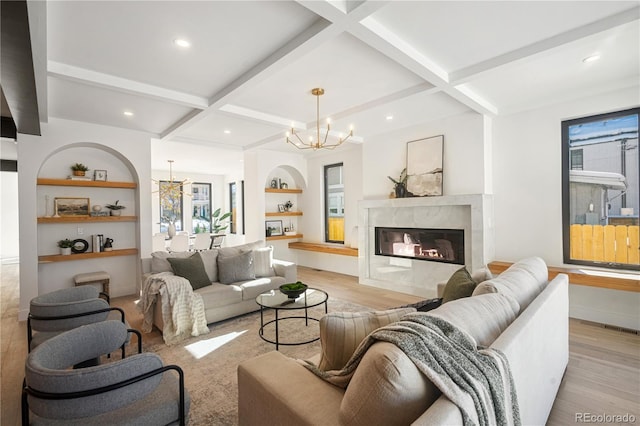 living room with beam ceiling, a chandelier, a high end fireplace, and light hardwood / wood-style floors