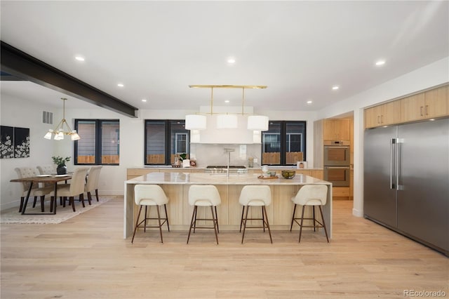 kitchen with stainless steel appliances, light brown cabinets, decorative light fixtures, an inviting chandelier, and light hardwood / wood-style floors